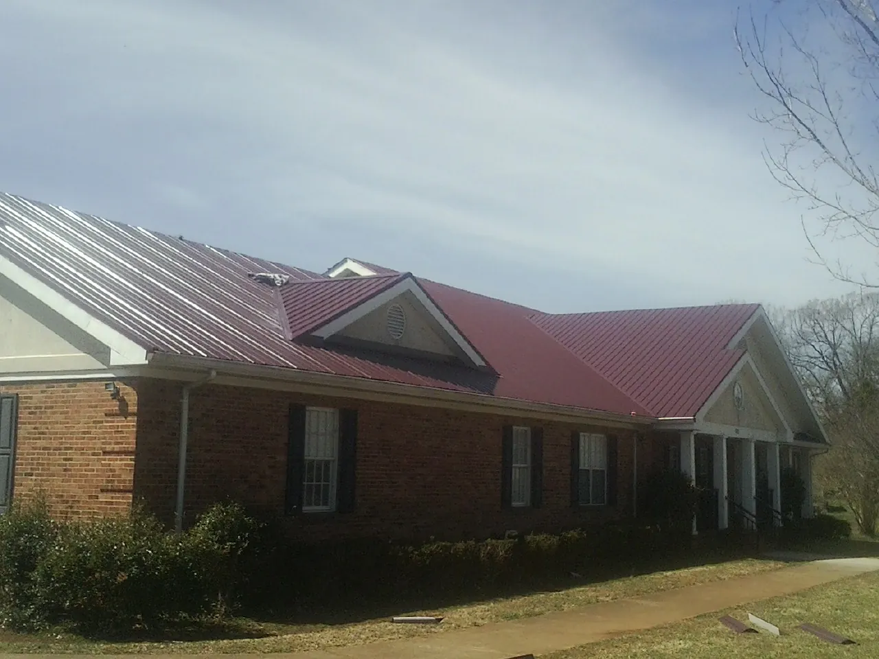 Red metal roof with gabled entries on a long brick building, from a Hail Damage Roof Repair job in Soap Lake