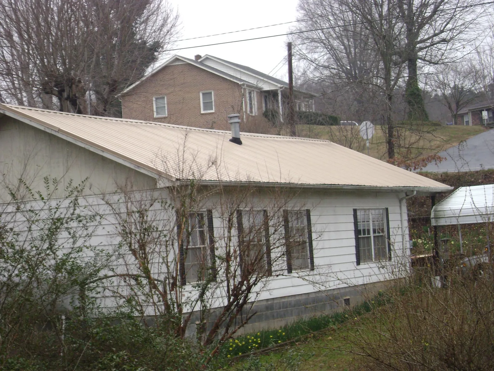 Tan metal roof on a white sided house set into a hillside — Commercial Roofing by Roofing Brothers in Soap Lake